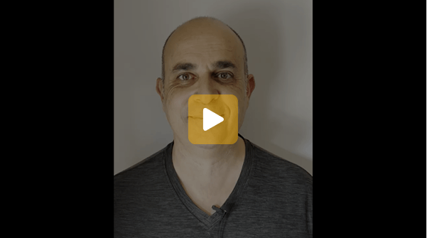 Video thumbnail: bald man in a dark shirt facing the camera with a neutral expression; centered play button overlays the image.