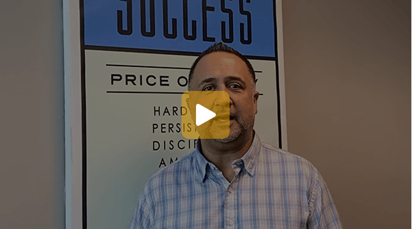 Video thumbnail: a man in a blue plaid shirt speaks in front of a poster that says SUCCESS, with words like persistence and discipline visible.