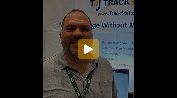 Man smiling at a TrackStat booth at a conference, wearing a gray polo and green lanyard.