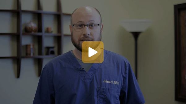 Video thumbnail: male clinician in blue scrubs speaking to the camera with a play button overlay on him.